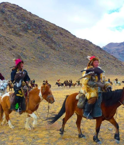 People on horseback wearing traditional attire, holding eagles in a vast, mountainous landscape.