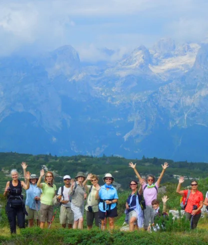 A group of people posing with hiking gear in a lush green landscape, with mountains and a cloudy sky in the background.