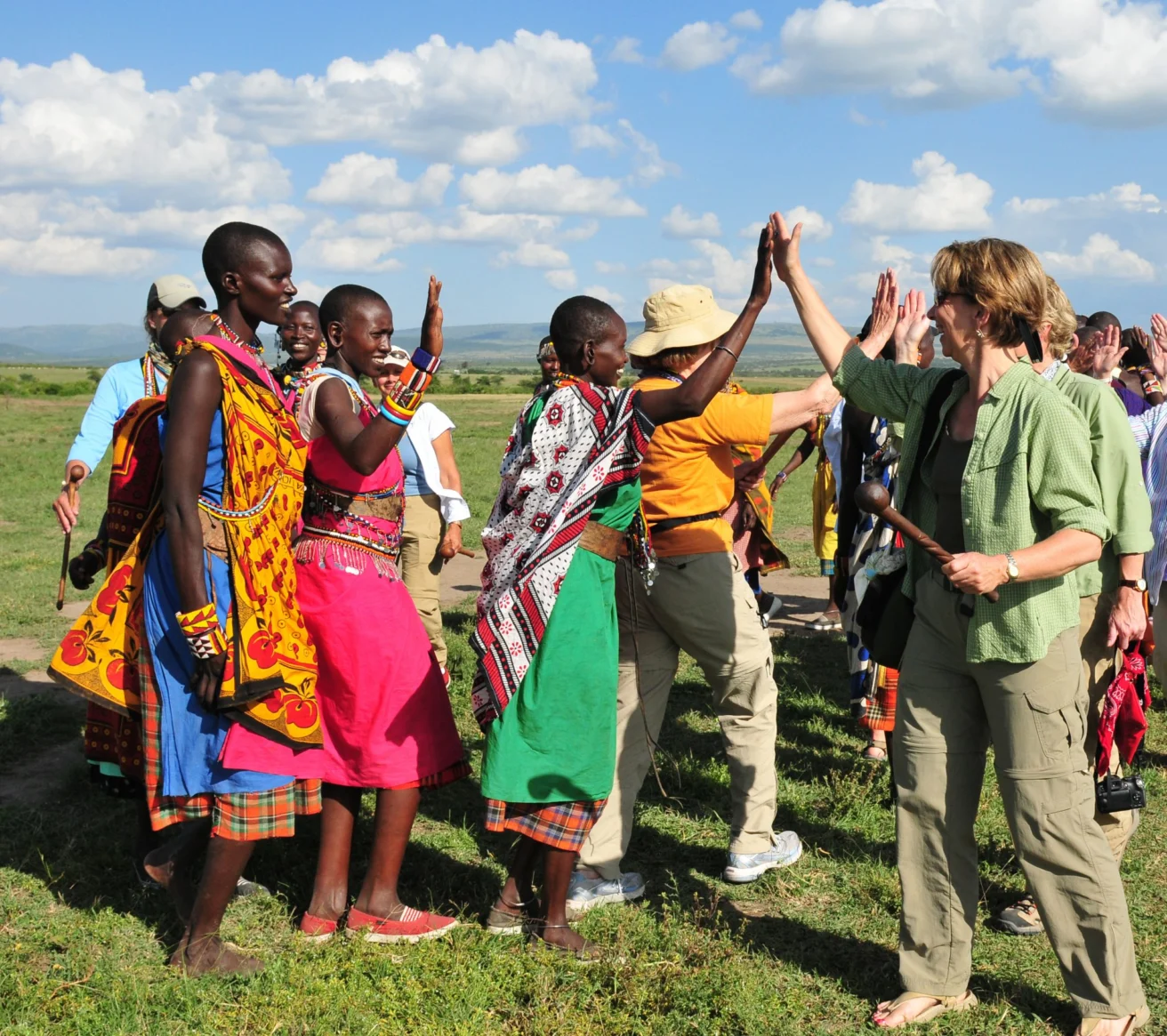 A group of people, including several in colorful traditional attire, share high-fives outdoors on a sunny day.