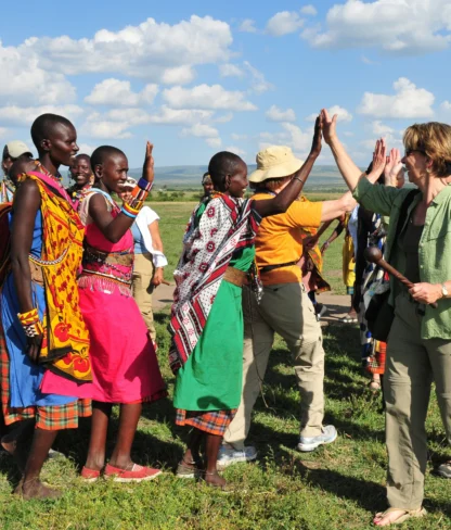 A group of people, including several in colorful traditional attire, share high-fives outdoors on a sunny day.