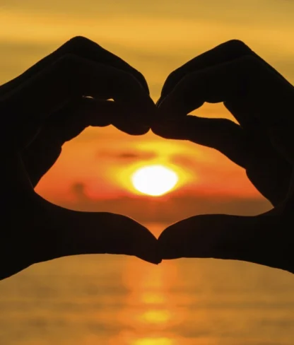 Silhouette hand in heart shape with sunset in the middle and ocean background