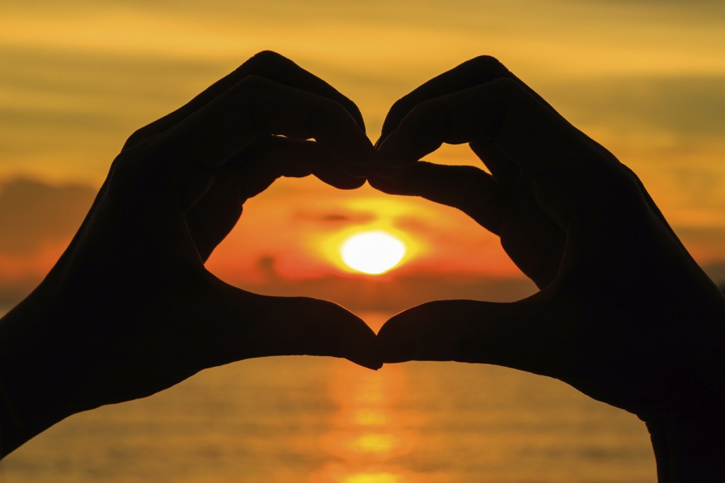 Silhouette hand in heart shape with sunset in the middle and ocean background