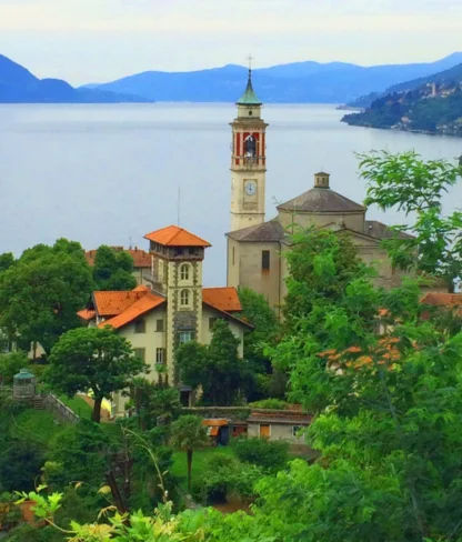 Scenic view of a lakeside village with a church tower, surrounded by lush greenery and mountains in the background.