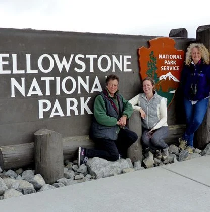 Four people pose by the Yellowstone National Park entrance sign, standing on a rocky surface.