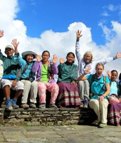 A group of people sitting on a stone wall, raising their hands against a backdrop of blue sky and clouds.