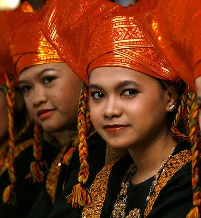 Four women wearing traditional orange headgear and black attire with gold accents, looking towards the camera.