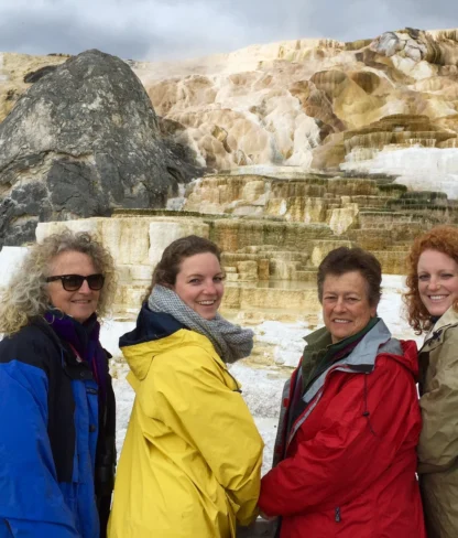 Four people in colorful jackets stand in front of layered geothermal terraces with rock formations in the background.