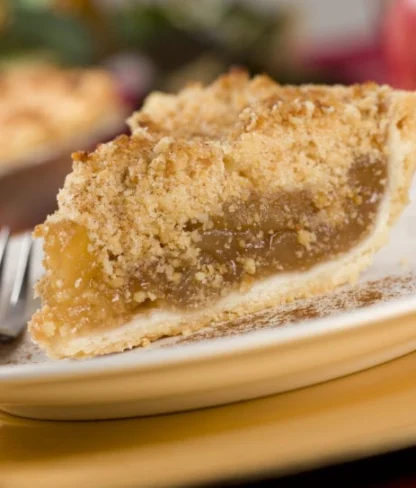 A slice of apple pie with crumb topping on a white plate with a fork beside it.