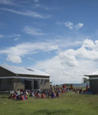 People gathered on grass outside two buildings under a blue sky with clouds.