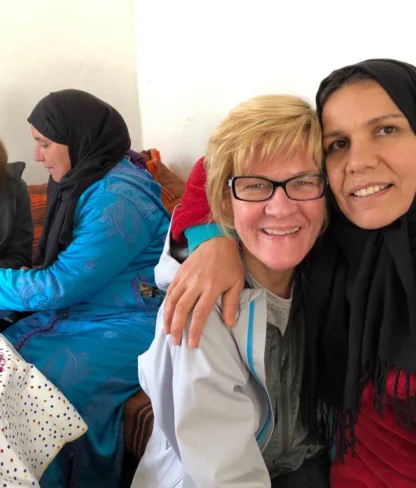 Four women sitting indoors, two smiling at the camera while one knits beside them.