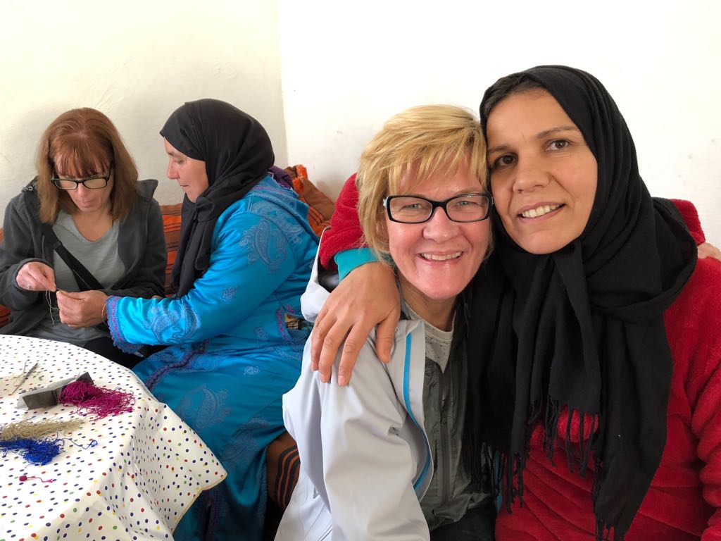 Four women sitting indoors, two smiling at the camera while one knits beside them.