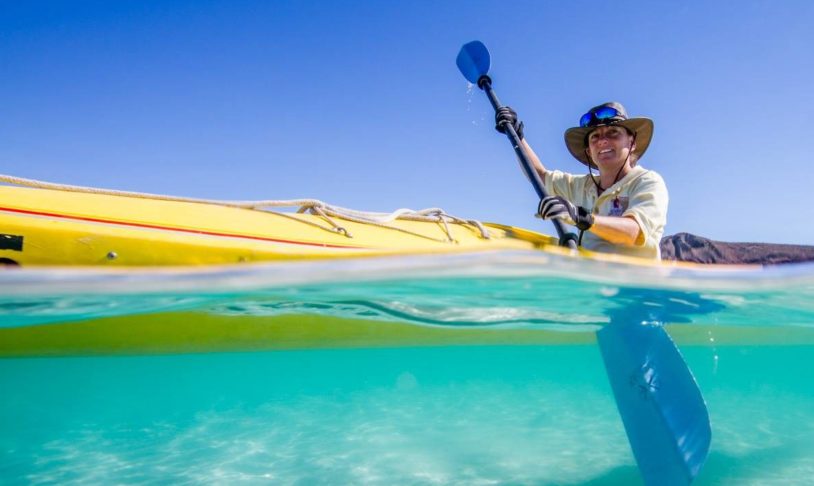 Adventurous woman kayaking in crystal clear ocean water in Baja