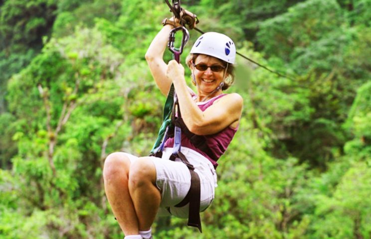 Close up of woman ziplining and smiling across trees.