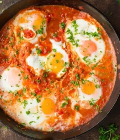 A skillet with shakshuka, featuring poached eggs in a spicy tomato sauce, garnished with chopped parsley.