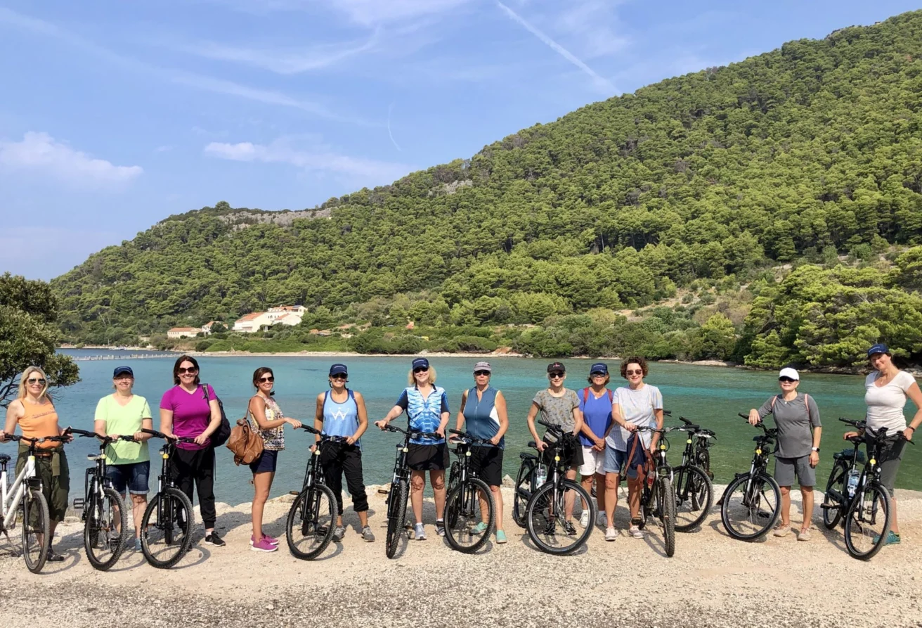 A group of people standing with bicycles in front of a scenic lake and forested hills.