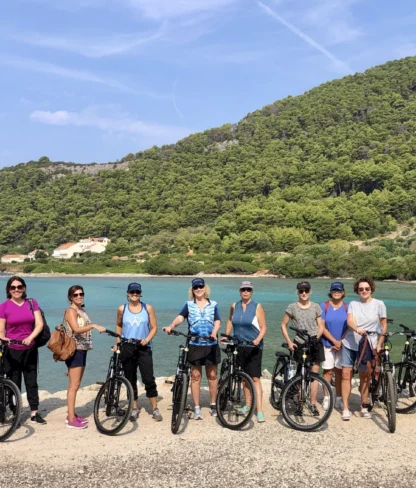 A group of people standing with bicycles in front of a scenic lake and forested hills.