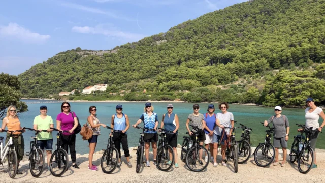 A group of people standing with bicycles in front of a scenic lake and forested hills.