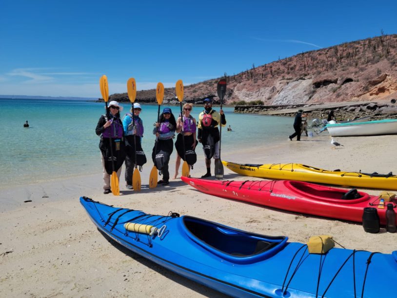 A group of women standing with kayaks and paddles ready to start their lesson