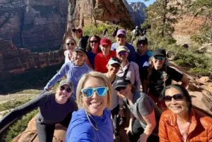 Group of people posing for a selfie on a rocky cliff with a scenic canyon view in the background.