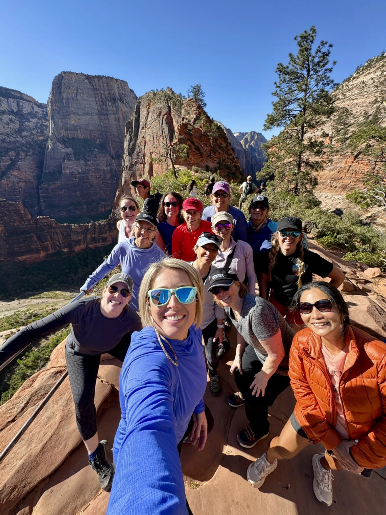 A group of people taking a selfie on a mountain trail with a scenic canyon view in the background.