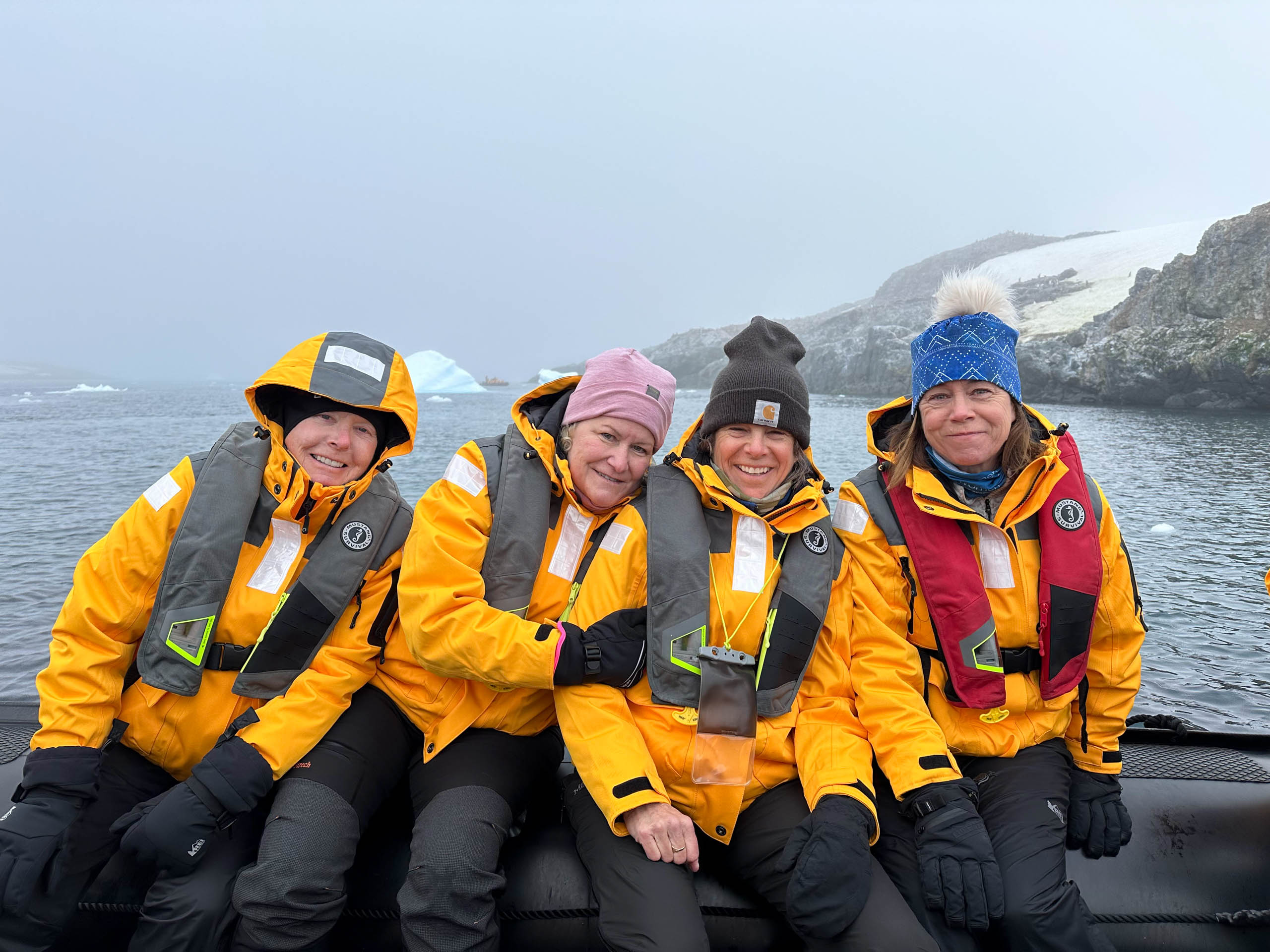 Four people in yellow jackets and life vests sit on a boat in a foggy, icy landscape.