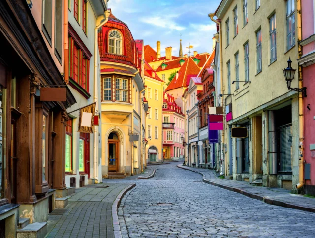 A narrow, colorful cobblestone street lined with historic buildings, featuring pastel facades and ornate architecture.