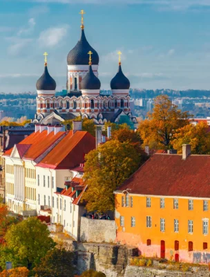 Colorful rooftops and medieval architecture of Tallinn, Estonia, with the Alexander Nevsky Cathedral and a tower visible against a clear sky.