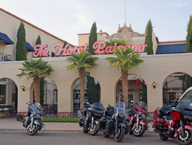 Line of motorcycles parked in front of The Hotel Paisano, with palm trees and an arched entrance.