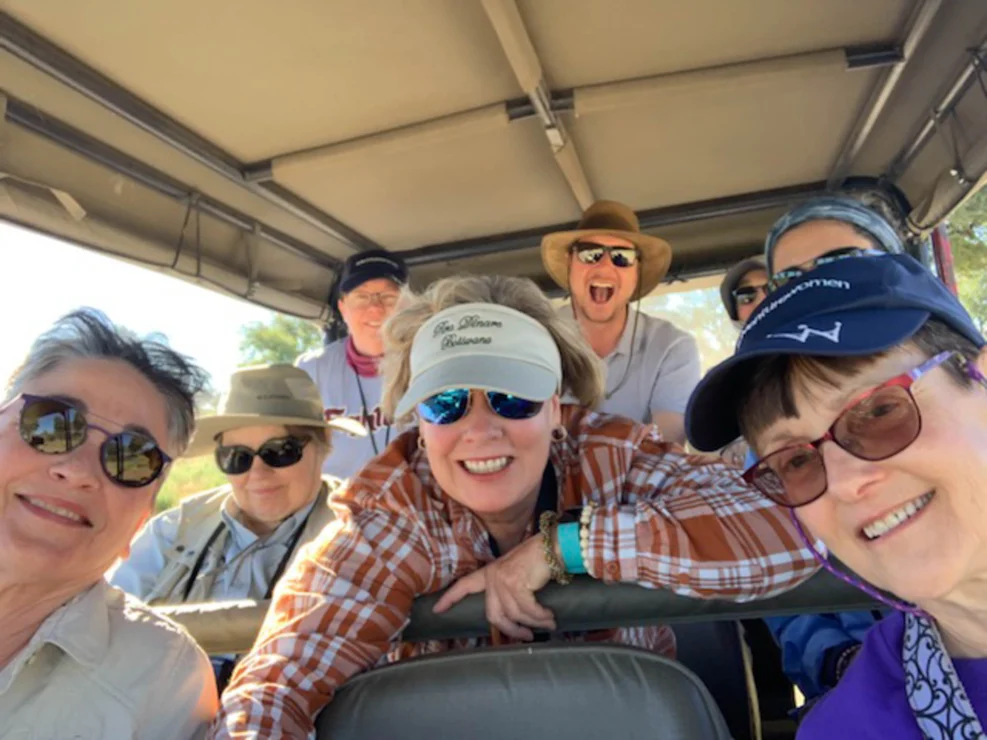 A group of people wearing hats and sunglasses smiles for a selfie inside an open vehicle during a sunny day.