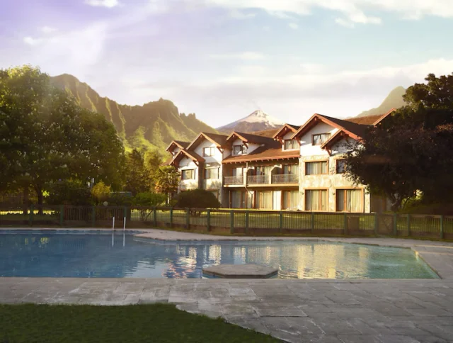 A row of chalet-style houses with red roofs near a mountainous landscape and a swimming pool in the foreground.