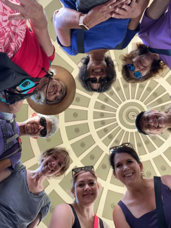 A group of people stand in a circle, looking down at the camera. Above them is a decorative domed ceiling.