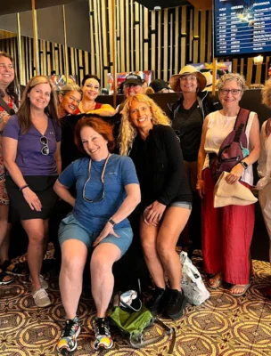 A group of ten people posing together indoors with a patterned carpet and a digital screen in the background.