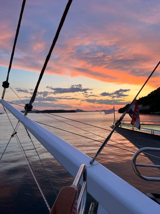 Sunset view from a boat, with vibrant orange and pink clouds reflecting on the water. Silhouetted islands are visible in the distance.