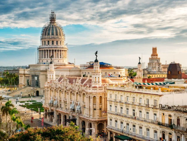 Aerial view of Havana with the Capitol building, historic architecture, and palm trees under a partly cloudy sky.