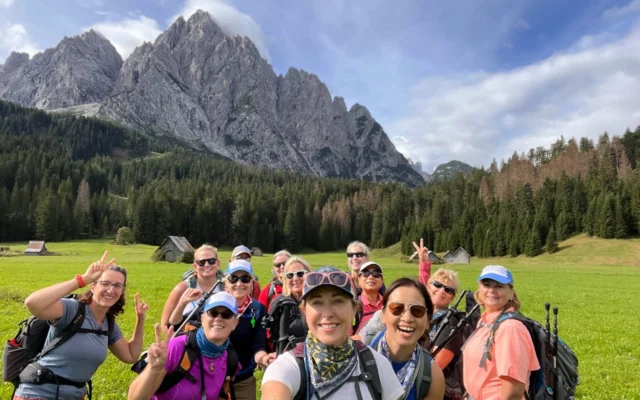 A group of hikers posing in a green field with mountains in the background on a sunny day.