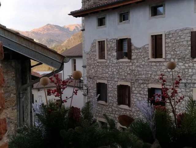 View of a stone building with shuttered windows, adorned with festive greenery and red berries in the foreground, with mountains visible in the distance.