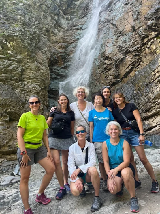 Group of eight people posing in front of a waterfall on a rocky hillside.