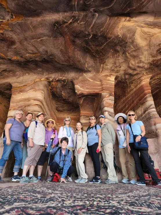 A group of people stands inside a rock formation with colorful striations on the walls and ceiling. There’s a patterned carpet on the ground.