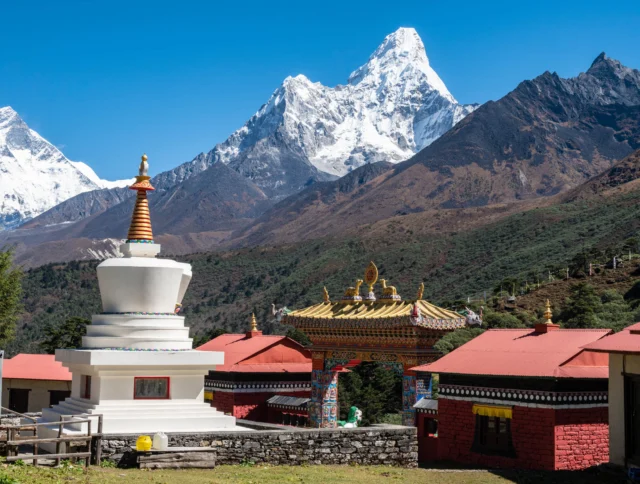 A mountain landscape with snow-capped peaks, a stupa, and a colorful gate. Buildings with red roofs are in the foreground.