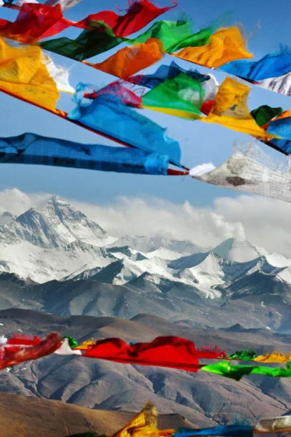 Colorful prayer flags flutter against a backdrop of snow-capped mountains and a clear blue sky.