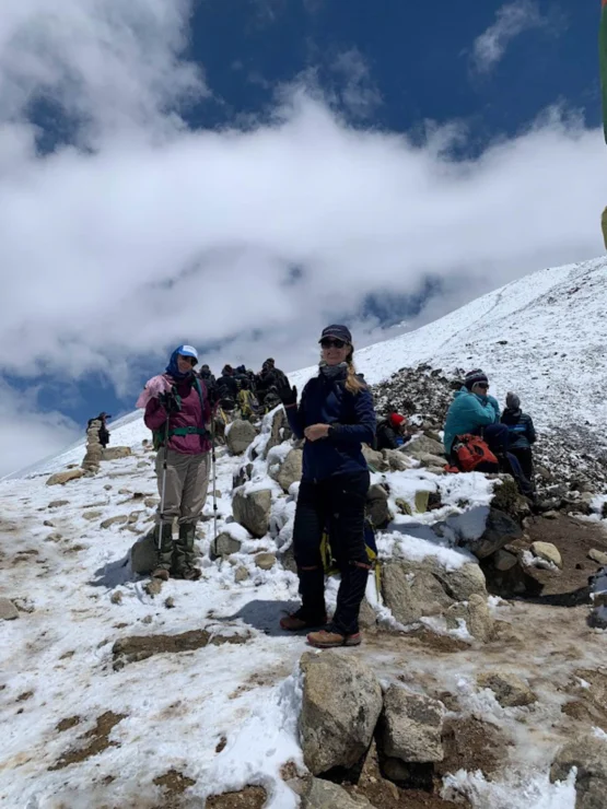 Several people in winter gear pause on a snowy mountain slope under a partly cloudy sky.