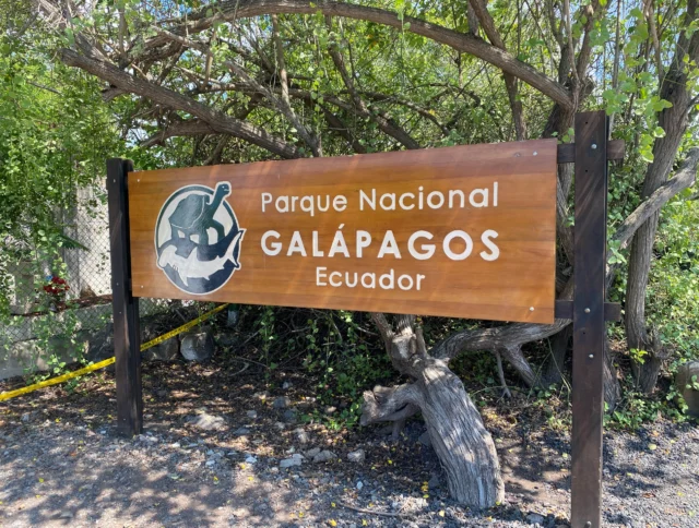 Sign for Parque Nacional Galápagos in Ecuador, surrounded by trees and vegetation.