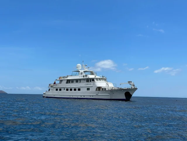 A large white yacht named "Coral I" is anchored on a calm blue sea under a clear sky.