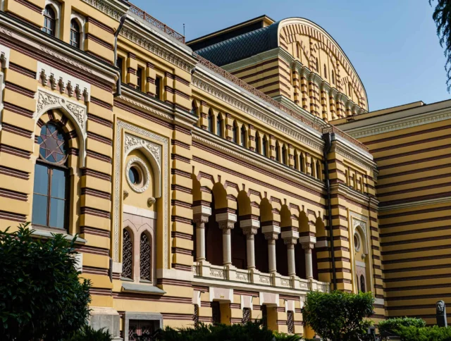 A historic building with ornate yellow and brown striped facade, arched windows, and balconies, set against a clear blue sky.