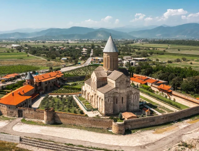 Aerial view of a historic stone cathedral surrounded by fortifications and green fields, with mountains in the background.