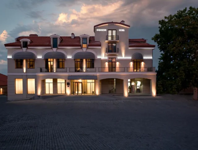 A three-story hotel building at dusk, with illuminated windows and a central tower, under a partly cloudy sky.