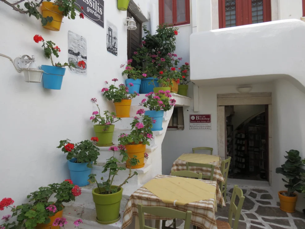 Outdoor cafe area with tables and chairs beside white stairs decorated with colorful potted flowers and plants.