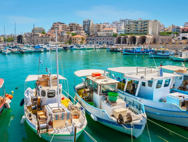 Fishing boats moored in a vibrant harbor with buildings in the background under a clear blue sky.