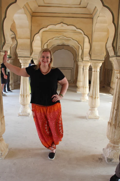 A person in a black shirt and red patterned pants leans against a pillar in an ornate stone hallway.