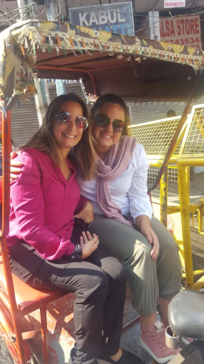 Two women sitting in a rickshaw, smiling and wearing sunglasses.